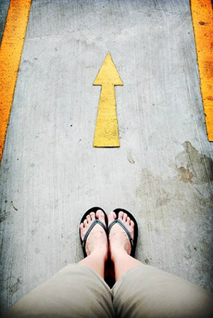 looking down at feet in flipflops standing in front of an arrow on the pavement pointing forward